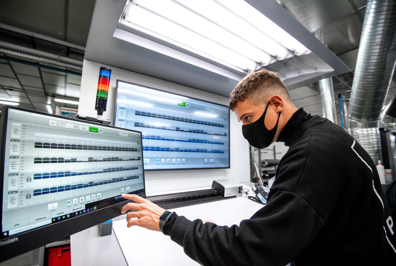 An operator at an offset press console, the ink-key screens of the closed loop in front of him